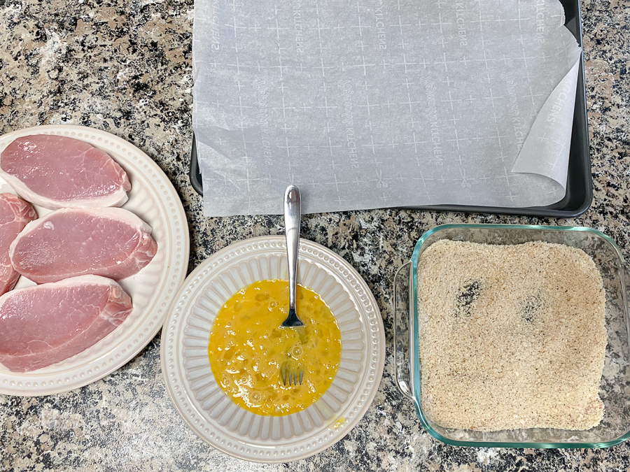Pork chop breading station with pork chops, egg mixture and bread crumb mixture