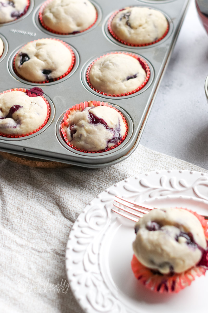 blueberry muffins in baking pan, with a plated muffin in the blurred foreground