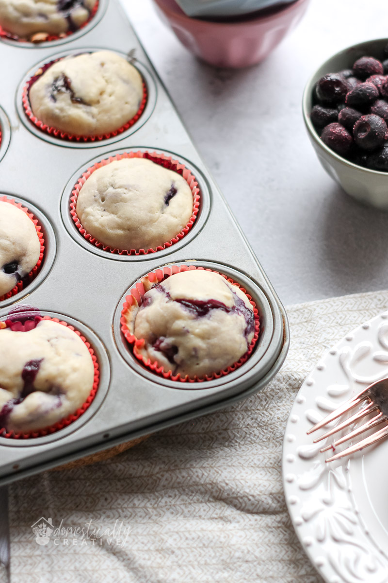 Blueberry muffins in a baking pan with blueberries in background