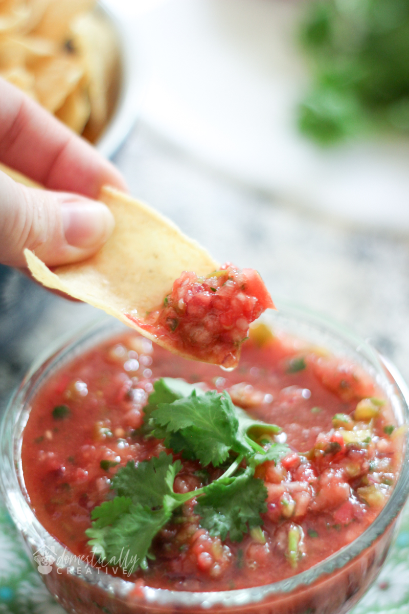 Homemade salsa with a hand holding tortilla chip dipped in the salsa bowl.