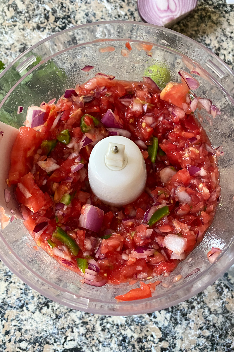 Lightly mixed tomato, onion and jalapeno in the bowl of a food processor