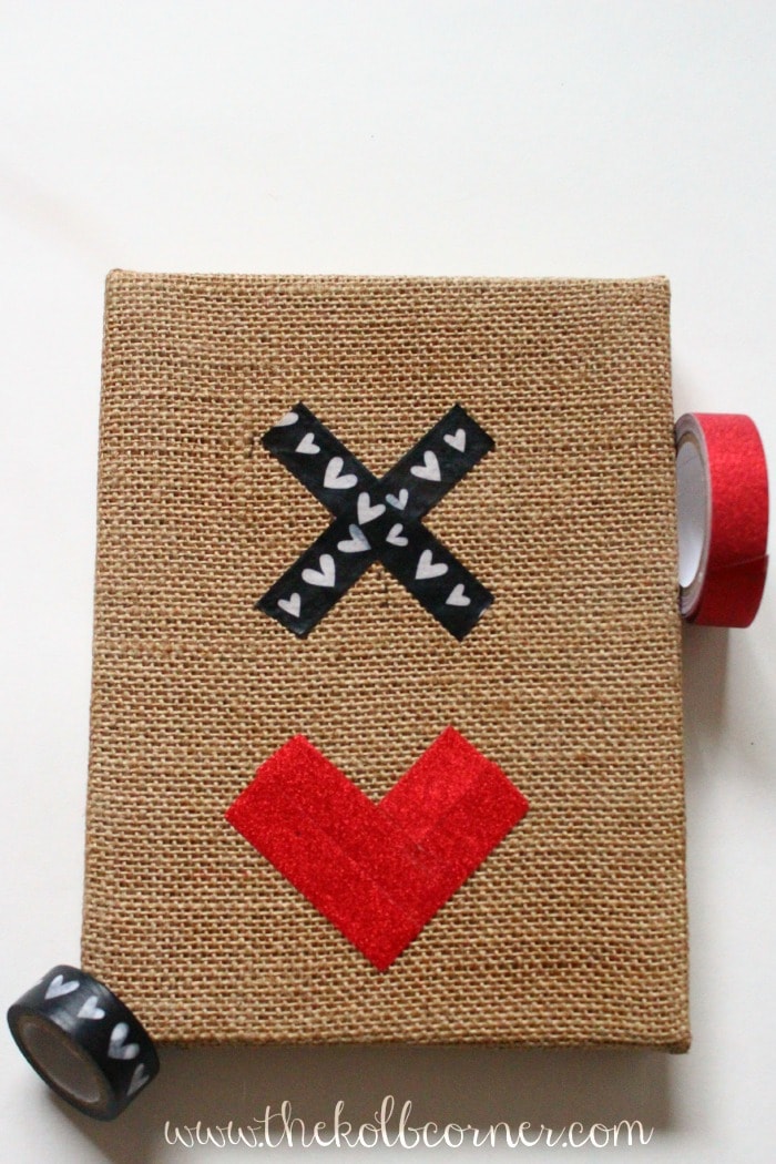 burlap canvas with black and white heart washi tape in "x" shape and glitter red washi tape in a heart shape.