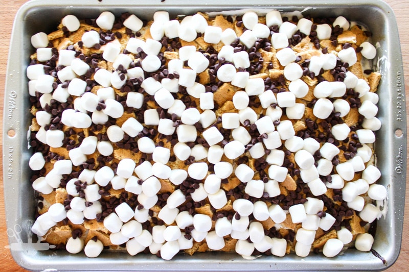 Overhead view of layered smores poke cake recipe topped with marshmallows chocolate chips and graham crackers