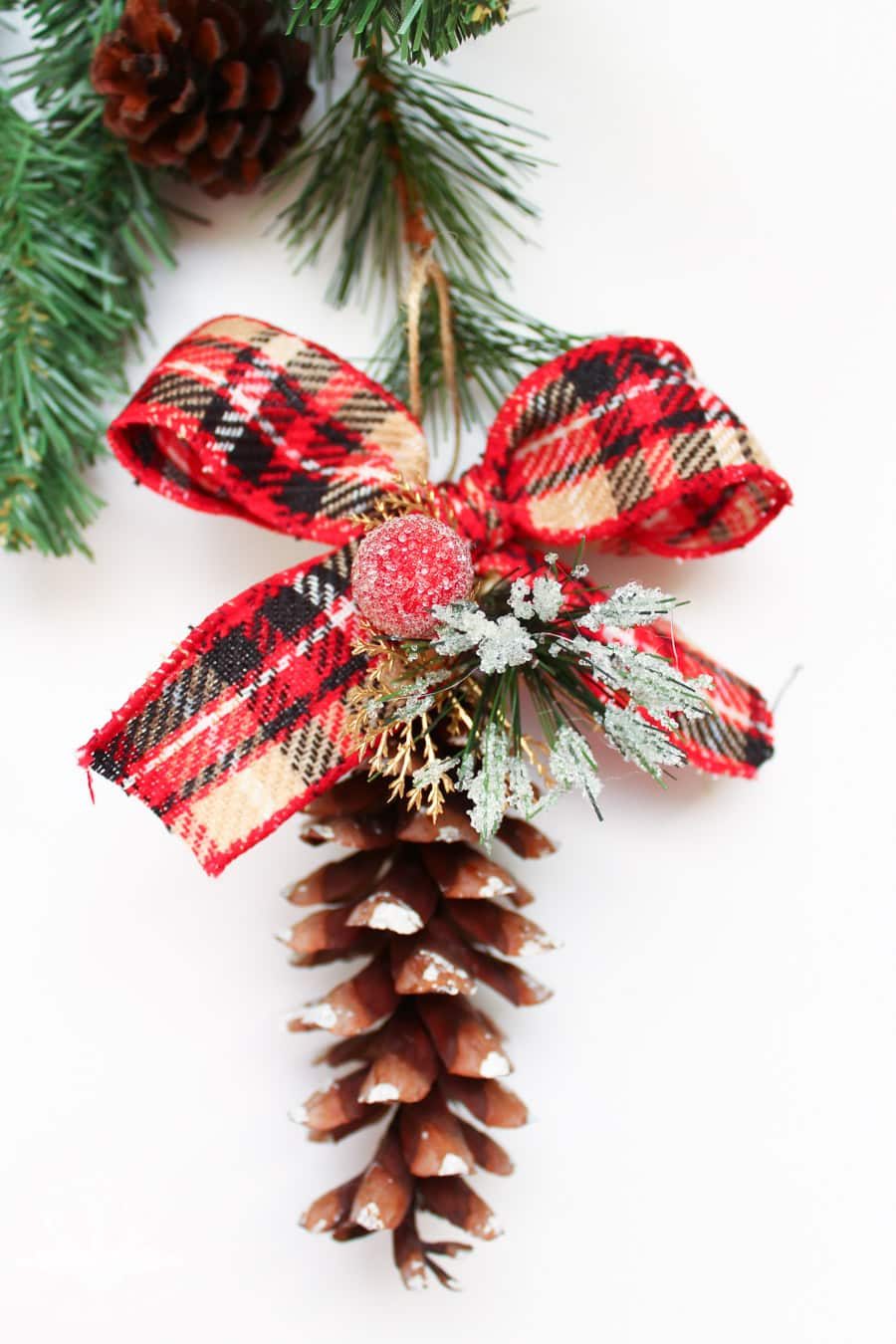 close up of pine cone ornament with a plaid bow and frosted red berries around the stem