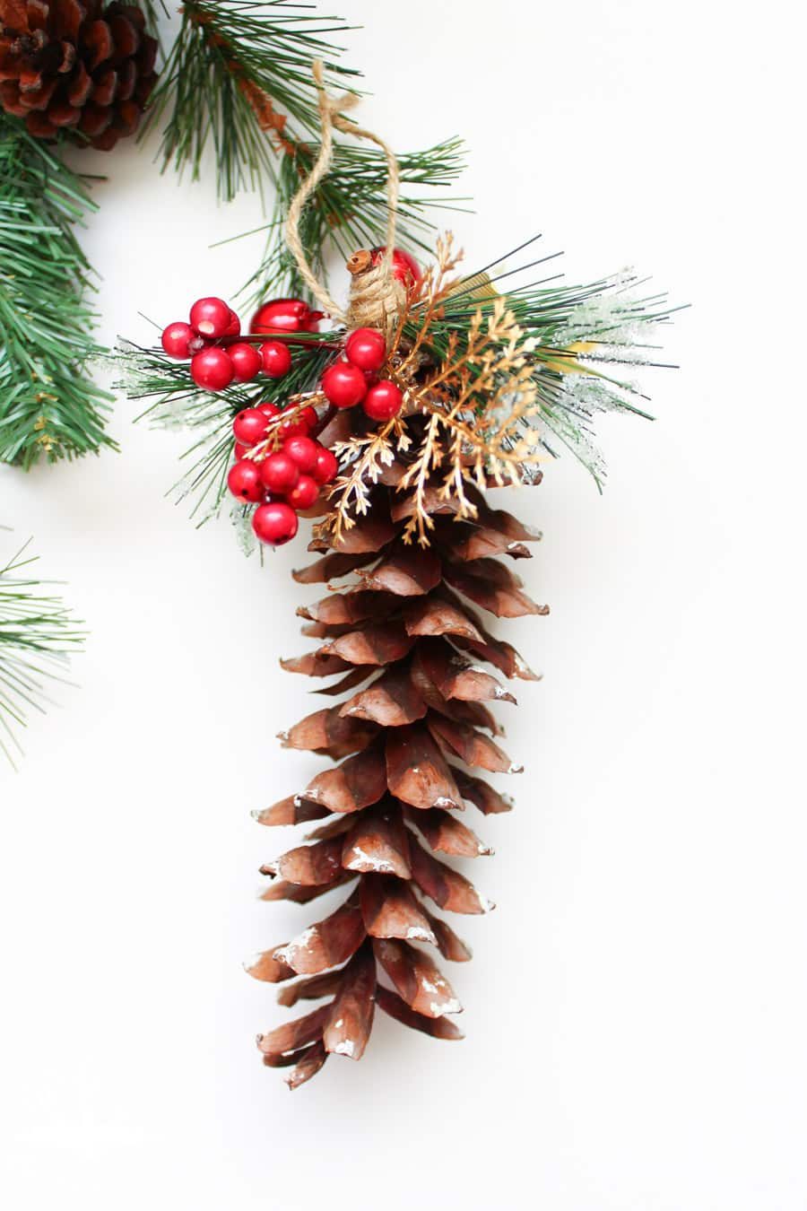close up of pine cone ornament with a red berries and gold leaves around the stem