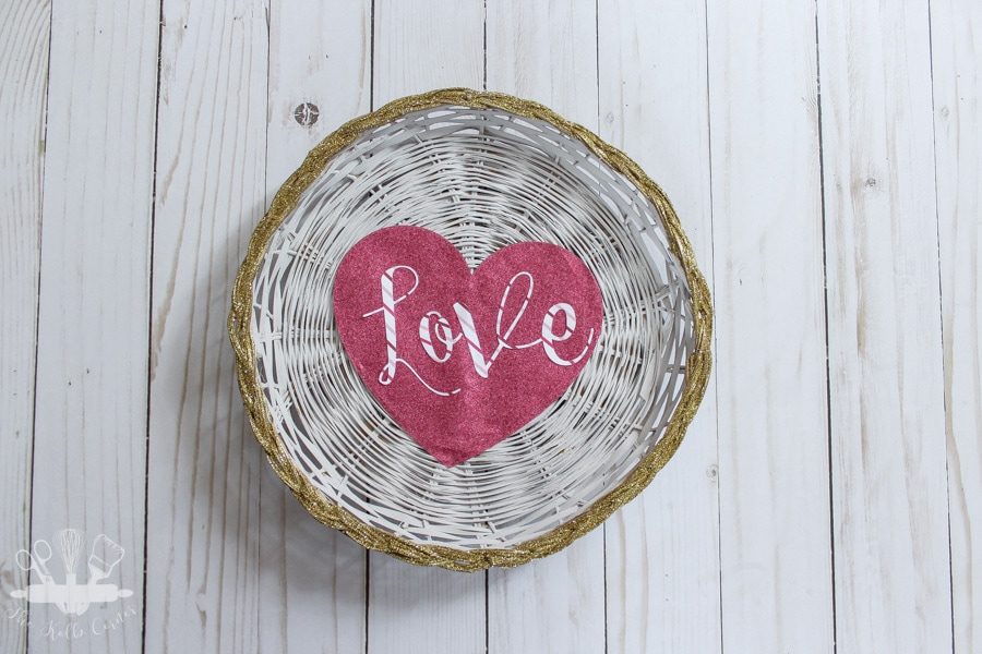 White painted wicker charger with gold glitter edge, pink glitter cardstock heart with the word "love" overlaid in pink stripe.