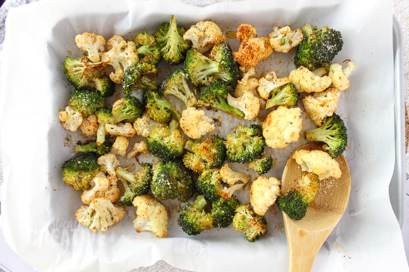 roasted cauliflower and broccoli florets on a baking pan with wooden spoon
