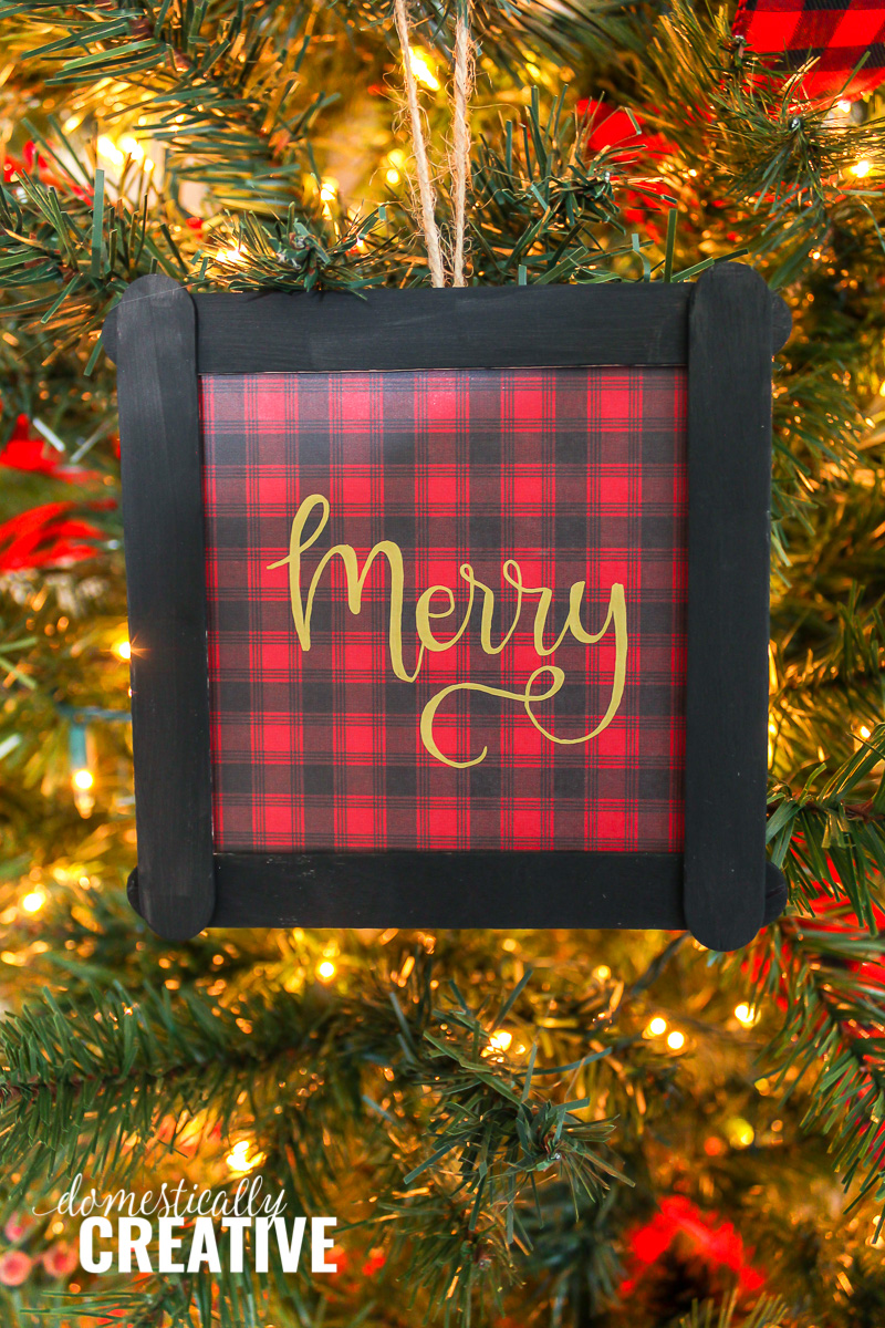 red and black plaid Christmas ornament with "Merry" hand lettered on Christmas tree background