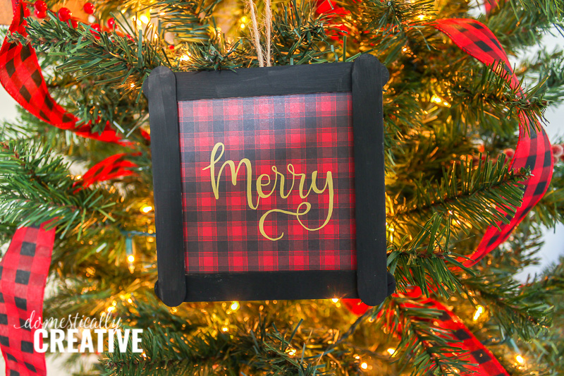 red and black plaid Christmas ornament with "Merry" hand lettered on Christmas tree background