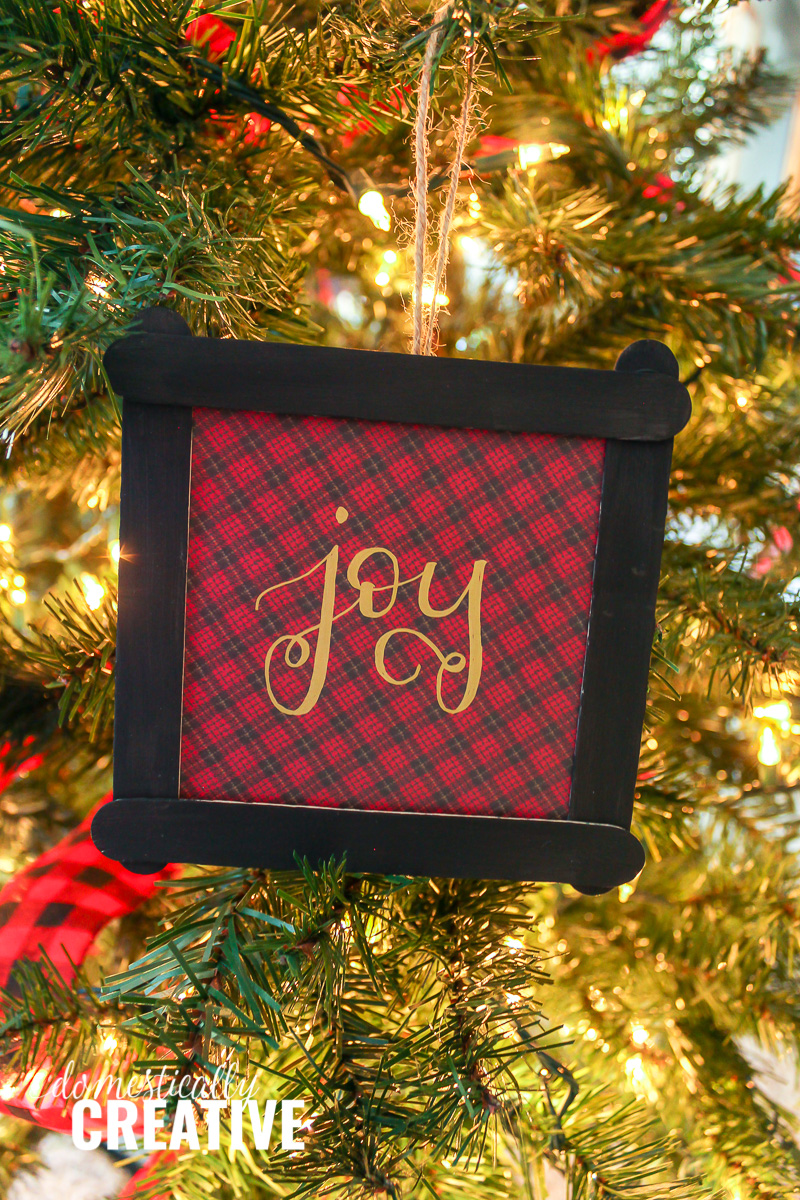 red and black plaid Christmas ornament with "joy" hand lettered on Christmas tree background