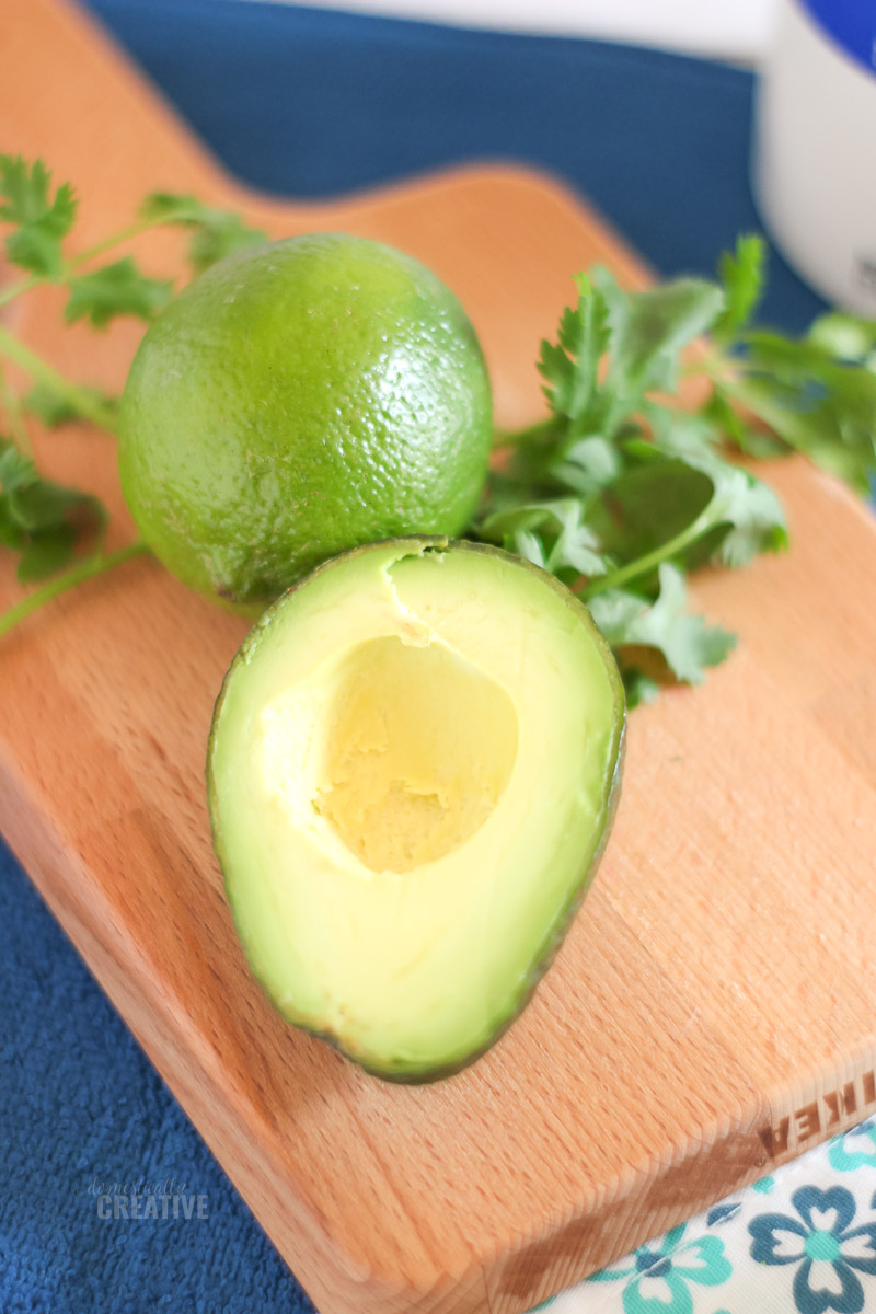 overhead slightly blurred photo of avocado, lime and cilantro on a wood cutting board