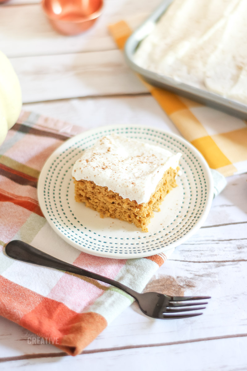 Close up Pumpkin bar on cake plate with back fork on a rustic white wood backdrop 