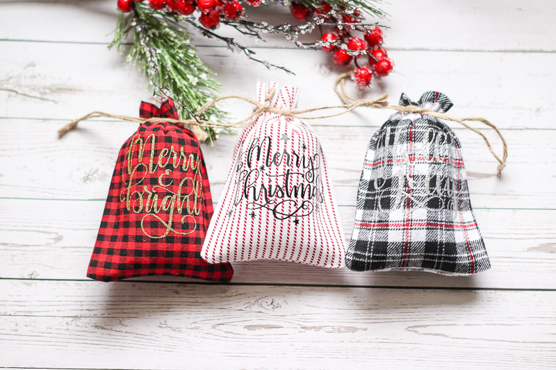 overhead of three drawstring Christmas patterned bags on white wood surface
