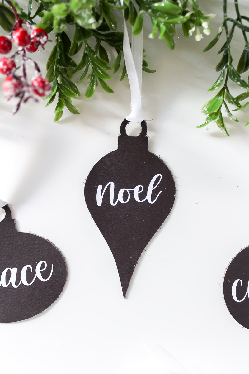 Noel leather ornament on white table with greenery