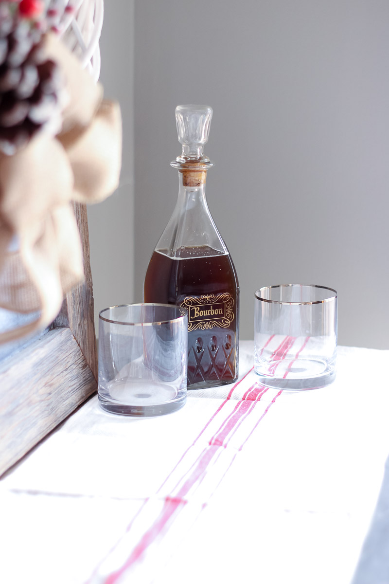 Vintage bourbon decanter with gold rimmed highball glasses on a red and white grain sack table runner