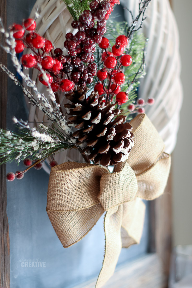 Close up of pinecone, red berries and frosted greenery with burlap bow
