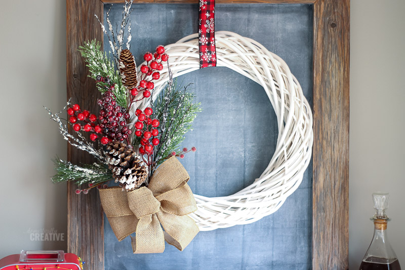 White wreath with red berries and greenery over a chalkboard