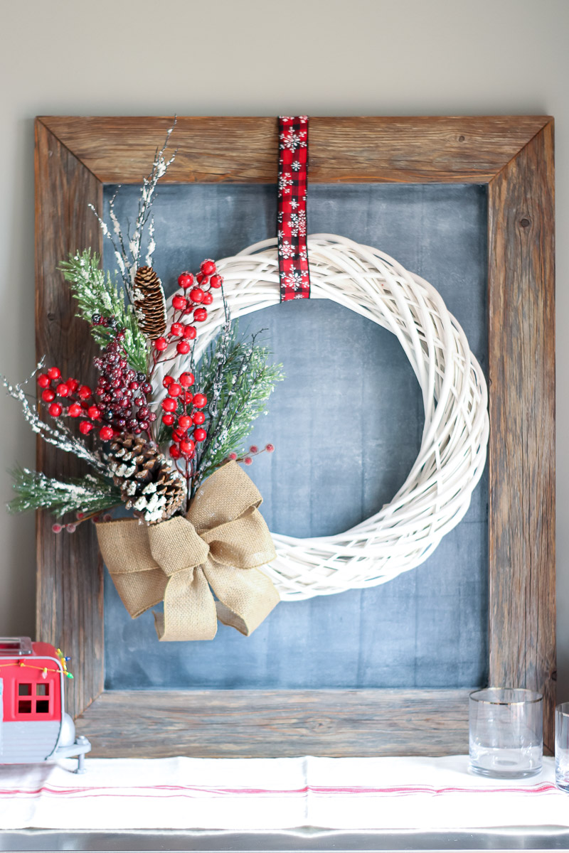 White wreath with red berries and greenery over a chalkboard