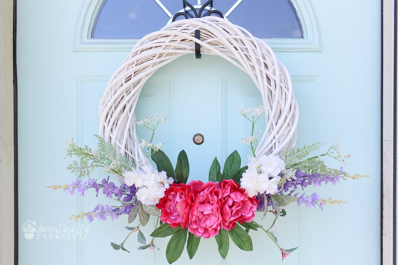 white wicker spring wreath with bright florals, on pastel door