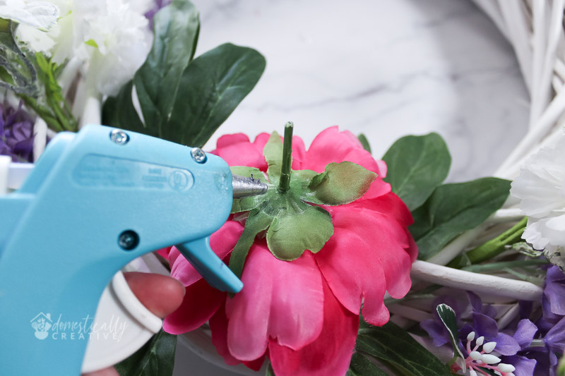 using a hot glue gun with peony floral to attach to wreath form